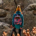 woman in brown knit cap and blue jacket standing on brown dried leaves during daytime