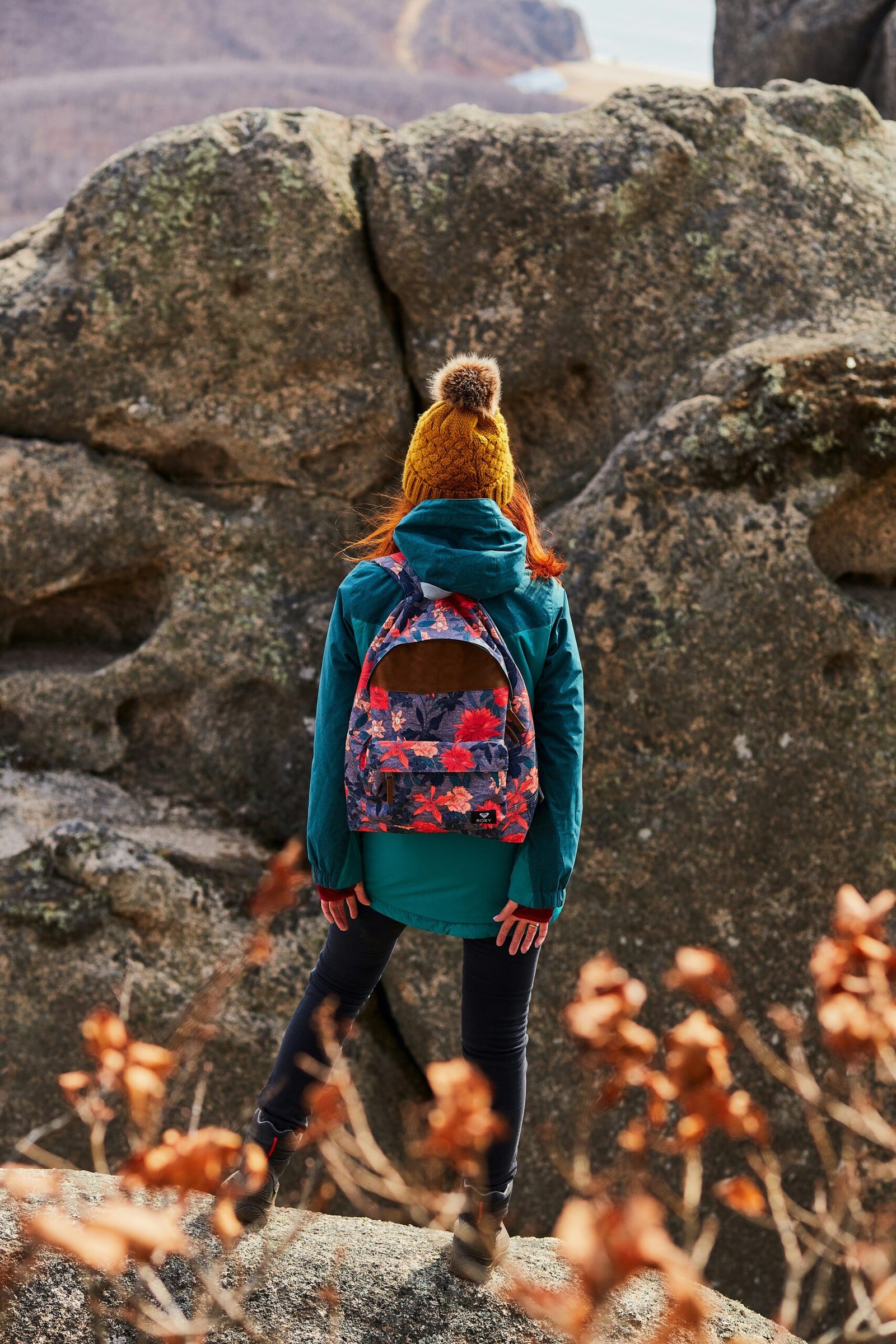 woman in brown knit cap and blue jacket standing on brown dried leaves during daytime